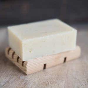 May include: A white bar of soap on a wooden soap dish. The soap is rectangular and has a slightly textured surface.
