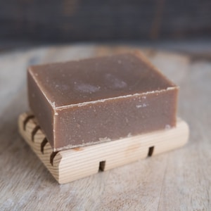 May include: A brown bar of soap on a wooden soap dish. The soap is rectangular and has a smooth surface.