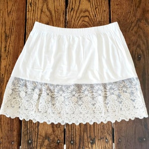 May include: White cotton slip skirt with a lace trim. The lace trim is a delicate floral pattern.