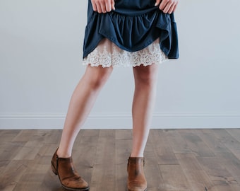 May include: A woman wearing a navy blue dress with a white lace trim and brown ankle boots.