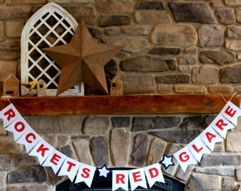 May include: A red, white, and blue banner with the text "ROCKETS RED GLARE" hanging above a fireplace. The banner is made of paper and has a star design on each flag.
