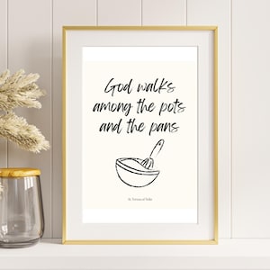 May include: A framed print with a white background and black text that reads "God walks among the pots and the pans."  The text is accompanied by a simple line drawing of a bowl and a whisk.  The quote is attributed to "St. Teresa of Avila".