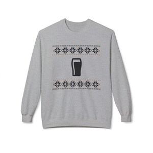Cozy holiday sweatshirt featuring a simple black pint glass design surrounded by festive knit-style snowflakes. Perfect for beer lovers, stout fans, and anyone who enjoys a classic winter look. Unisex white or gray sweatshirt with a soft, brushed interior and relaxed fit — ideal for Christmas parties, pub nights, or lounging by the fire. Eco-friendly materials and durable design for lasting comfort and holiday cheer. Keywords: guinness christmas sweater, beer lover gift, beer christmas gift