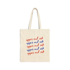 May include: A natural-colored tote bag with the phrase "upper cast side" repeated five times in red and blue lettering.