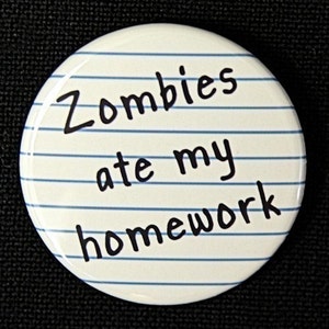 May include: A white button with blue lines resembling notebook paper. The text "Zombies ate my homework" is written in black.