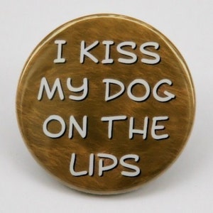 May include: A gold-colored round button with the text "I kiss my dog on the lips" in white.