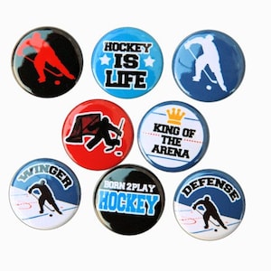 May include: Eight round hockey-themed buttons with various designs.  The buttons feature hockey players, hockey sticks, and text such as "Hockey is Life", "Born 2 Play Hockey", and "King of the Arena".