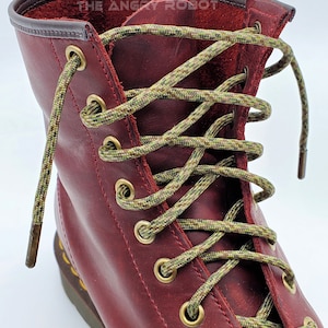 May include: Close-up of a pair of red leather boots with green and brown camouflage shoelaces. The laces are tied in a criss-cross pattern and the boots have gold eyelets.
