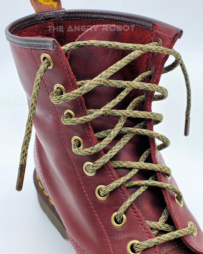 May include: Close-up of a pair of red leather boots with green and brown camouflage shoelaces. The laces are tied in a criss-cross pattern and the boots have gold eyelets.