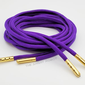 May include: Purple shoelaces with gold aglets. The shoelaces are coiled and the aglets are visible.