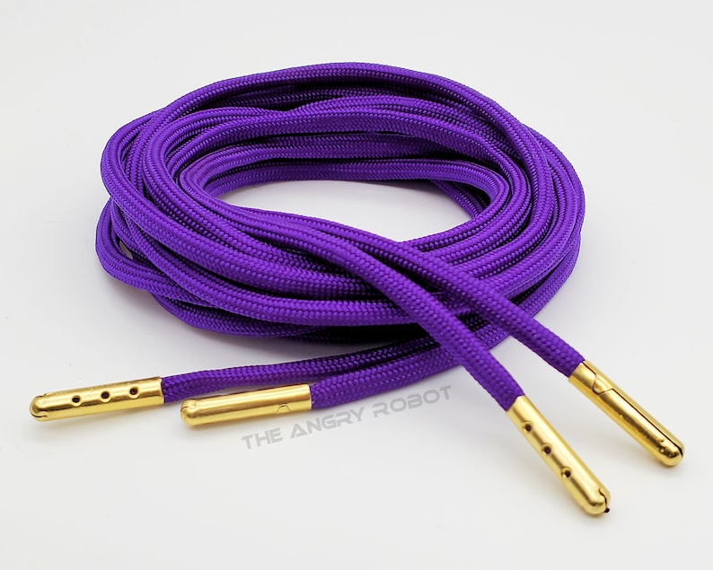May include: Purple shoelaces with gold aglets. The shoelaces are coiled and the aglets are visible.
