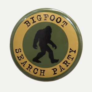 May include: A green button with a gold border and the text "BIGFOOT SEARCH PARTY" in black. A silhouette of Bigfoot is in the centre of the button.