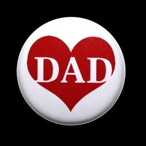 May include: White button with a red heart and the word "DAD" in white letters.