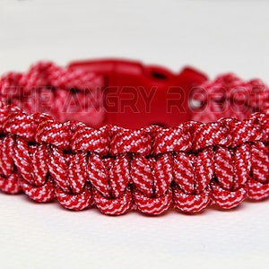 May include: Red and white paracord bracelet with a black plastic buckle. The bracelet is woven in a pattern that resembles a cobra weave.
