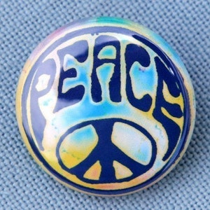 May include: A round, blue and yellow peace sign button with the word "PEACE" in a stylized font.