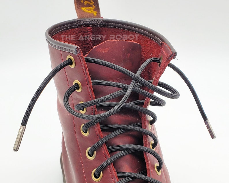 May include: Close-up of a pair of red leather boots with black shoelaces. The laces are threaded through metal eyelets and have metal aglets at the ends. The text "THE ANGRY ROBOT" is visible on the boot.