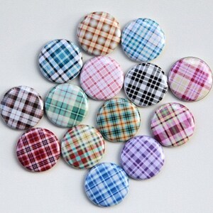 Puede incluir: Doce botones redondos con diferentes patrones de cuadros. Los botones son de varios colores, incluyendo azul, verde, rojo, rosa y marr&oacute;n.