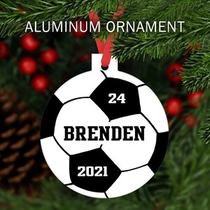 May include: White and black soccer ball Christmas ornament with the name "Brenden" and the number "24" printed on it. The year "2021" is also printed on the ornament.