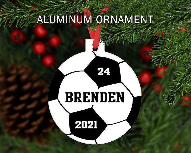 May include: White and black soccer ball Christmas ornament with the name "Brenden" and the number "24" printed on it. The year "2021" is also printed on the ornament.