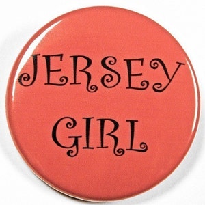 May include: A round, coral-colored button with the text "JERSEY GIRL" in black, curly font.