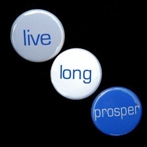 May include: Three round buttons with the words "live", "long", and "prosper" printed in white on a blue background.