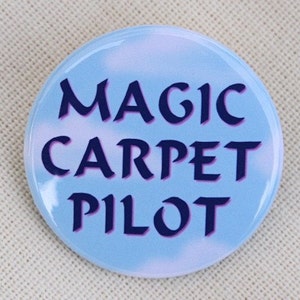May include: A blue button with a white cloud design. The text "MAGIC CARPET PILOT" is printed in dark blue.