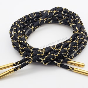 May include: Black and gold shoelaces with gold metal aglets. The shoelaces have a woven pattern.