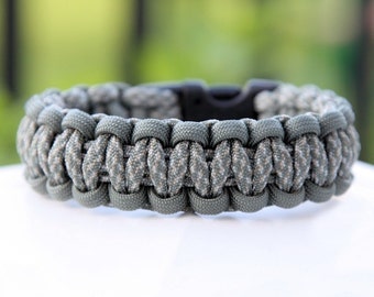 May include: A gray and white camouflage paracord bracelet with a black plastic buckle.