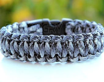 May include: A black and gray camouflage paracord bracelet with a black buckle.
