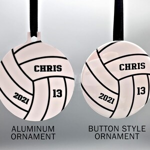 May include: Two white volleyball ornaments with black stitching and black text. The ornament on the left is labeled "Aluminum Ornament" and the ornament on the right is labeled "Button Style Ornament". Both ornaments have the text "CHRIS 13 2021" on them.