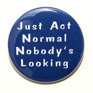 May include: A blue round button with white text that reads "Just Act Normal Nobody's Looking".