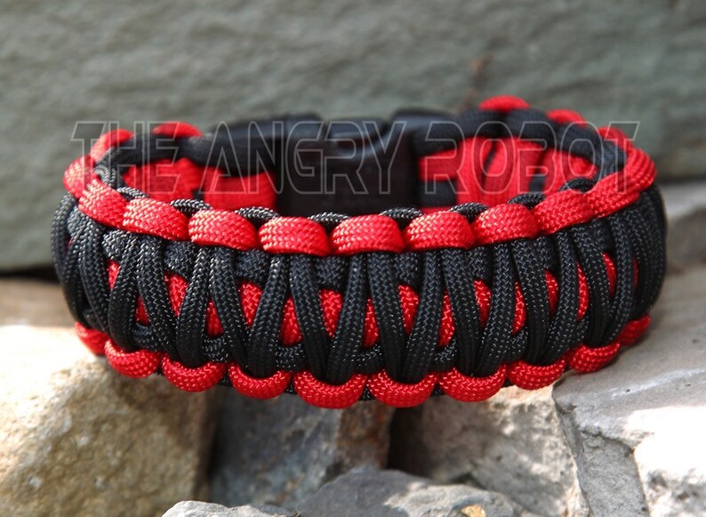 Puede incluir: Pulsera de paracord negra y roja con una hebilla negra. La pulsera est&aacute; hecha con un patr&oacute;n de tejido cobra.