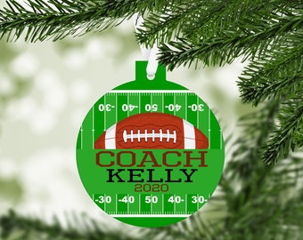 May include: Green and brown round Christmas ornament with a football and the text "COACH KELLY 2020" on a green field background.