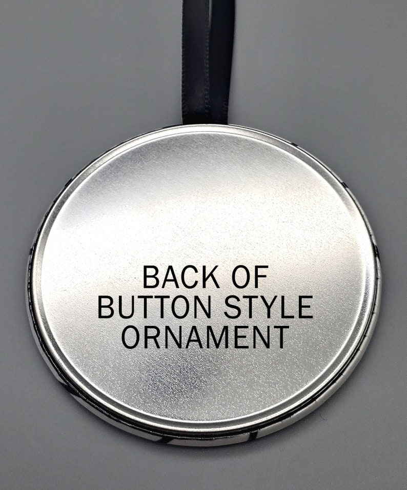 May include: The back of a round, silver button-style ornament with a black ribbon attached. The ornament has the text "BACK OF BUTTON STYLE ORNAMENT" printed on it.