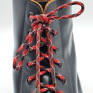 May include: Black leather boots with red, white, and black shoelaces. The laces are tied in a criss-cross pattern and secured with silver metal lace locks.