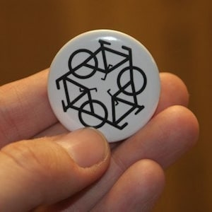 May include: A white button with a black design of five bicycles stacked on top of each other.