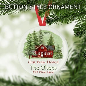May include: A white round Christmas ornament with a watercolor illustration of a red house with green trees and the text "2024 Our New Home The Olsens 123 Pine Lane"