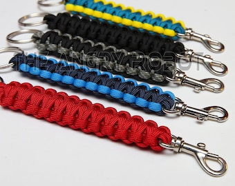 Puede incluir: Cinco llaveros de paracord de colores vivos con anillas y mosquetones plateados. Los llaveros son rojo, azul, negro, gris y amarillo.