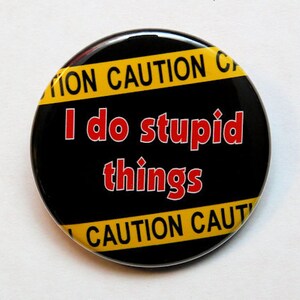 May include: Black and yellow round button with the text "Caution" and "I do stupid things" in red.
