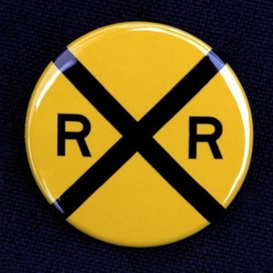 May include: A yellow round railroad crossing sign with a black X and the letters RR in black.