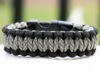 May include: A black and green camouflage paracord bracelet with a black plastic buckle.