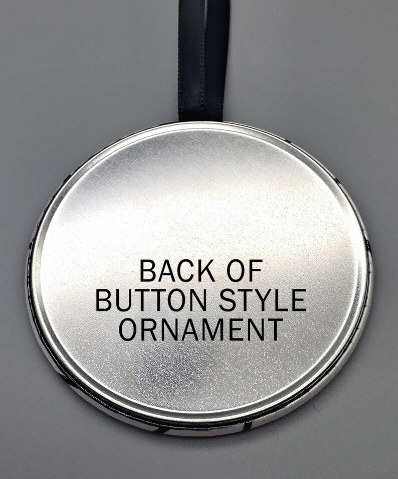 May include: The back of a silver round button style ornament with a black ribbon attached. The text "BACK OF BUTTON STYLE ORNAMENT" is printed on the back of the ornament.