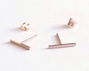 May include: A pair of rose gold bar stud earrings. The earrings are simple and minimalist, with a straight bar design.