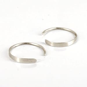 Op de afbeelding: Twee zilveren oorringen met een plat, breed bandje. De oorringen zijn simpel en minimalistisch.