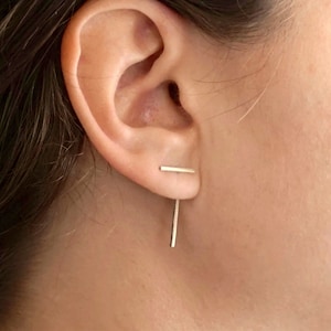 May include: A pair of silver bar earrings. One earring is a short horizontal bar, and the other is a longer vertical bar.