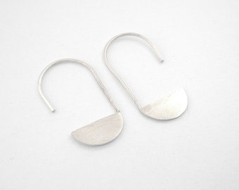 Puede incluir: Un par de pendientes de plata con forma de semicírculo. Los pendientes son simples y modernos en diseño.