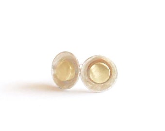 May include: A pair of silver stud earrings with a small, round, gold disc in the center.