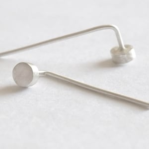 May include: A pair of silver stud earrings with a small, round disc at the end of each post.