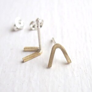May include: A pair of gold and silver earrings with a simple geometric design. The earrings are shaped like an upside-down V and a small arch.