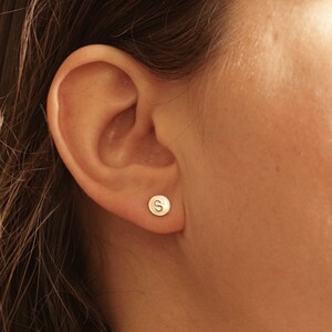 May include: A close-up of a person's ear with a small gold earring featuring the letter "S".